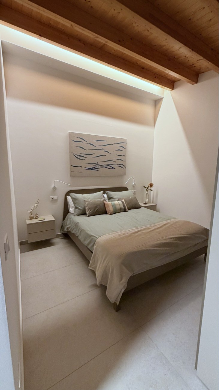 Studio Secondo bedroom with wood-beam ceiling and a painting of sardines above the bed