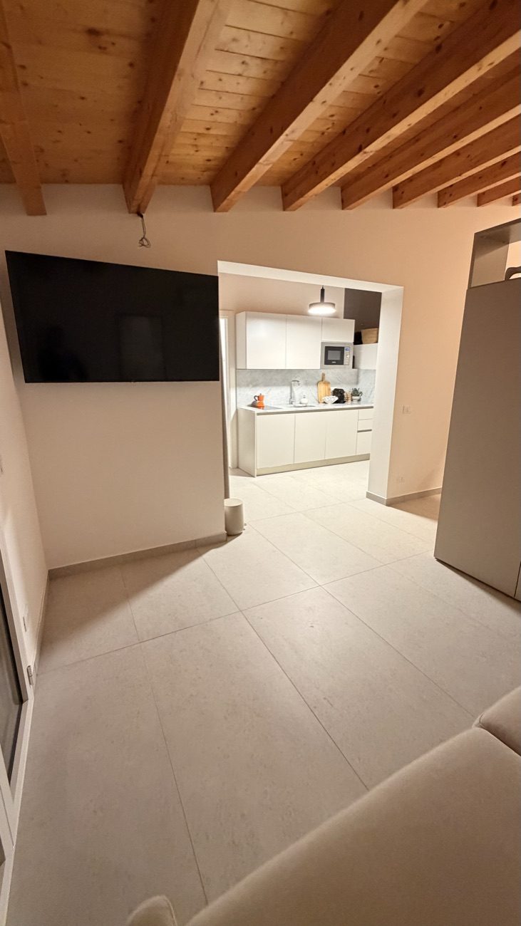 Studio Secondo living area with a wall-mounted 55-inch smart TV and the kitchen beyond